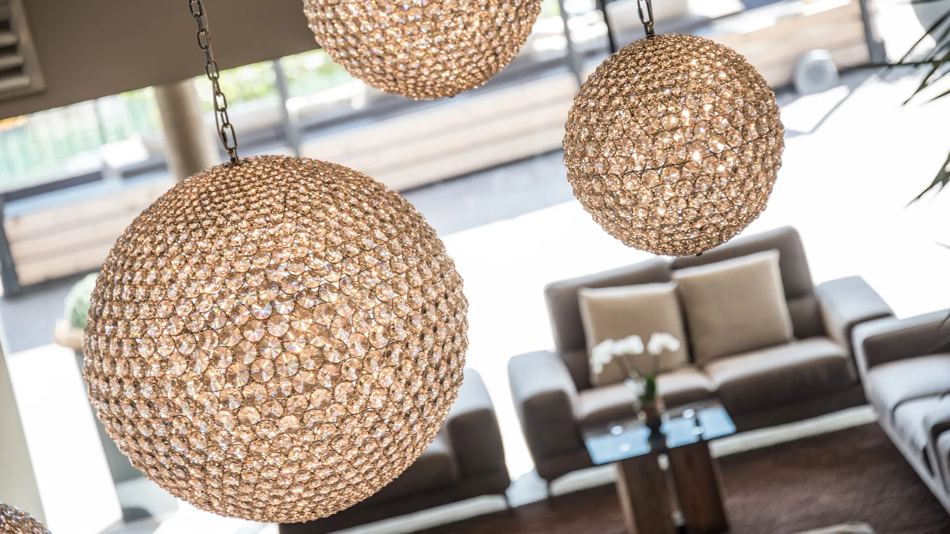 Funkelnde Kristall-Kugelleuchten in Gold-Champagner mit eleganter Lounge-Sitzgruppe und Fensterfront